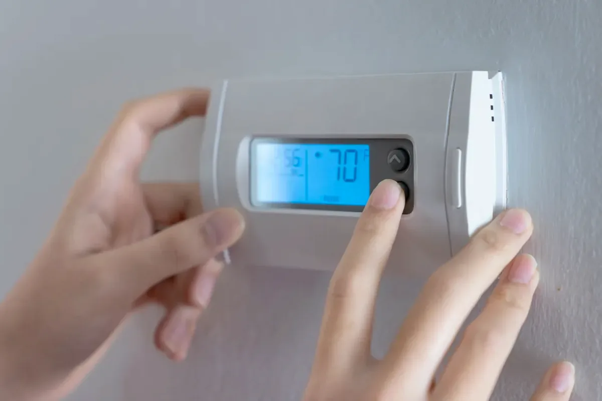 Hands adjusting a digital wall thermostat