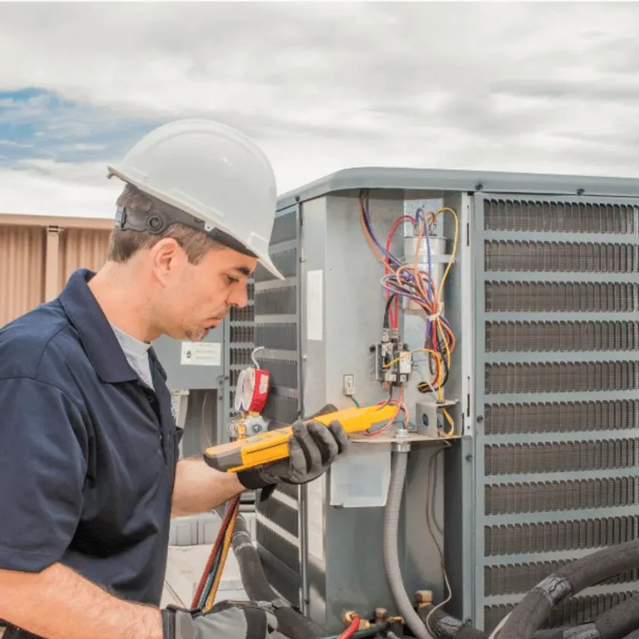 HVAC technician in a hard hat testing an outdoor air conditioner with a multimeter